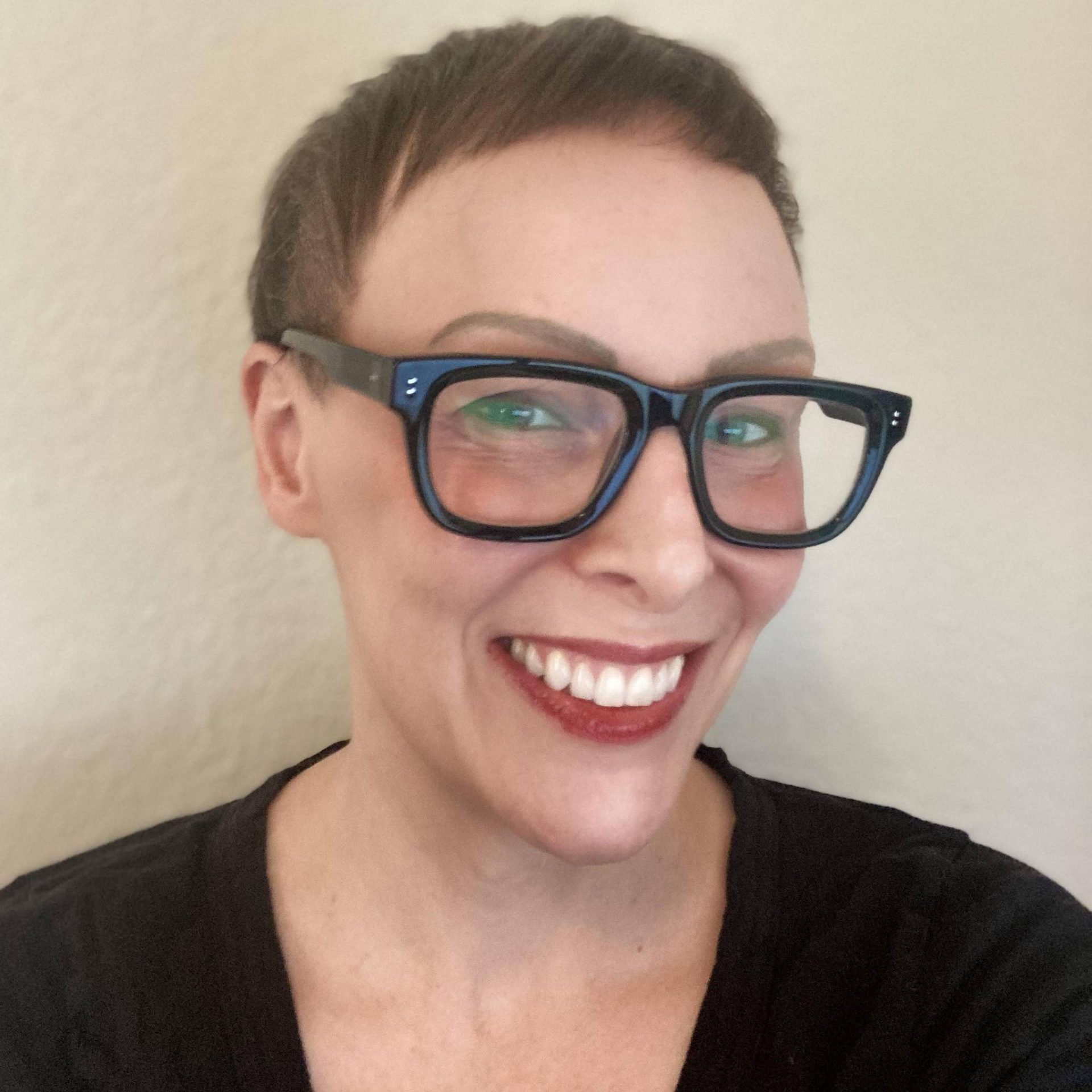 a woman with short brown hair wearing black glasses and a black t shirt is smiling